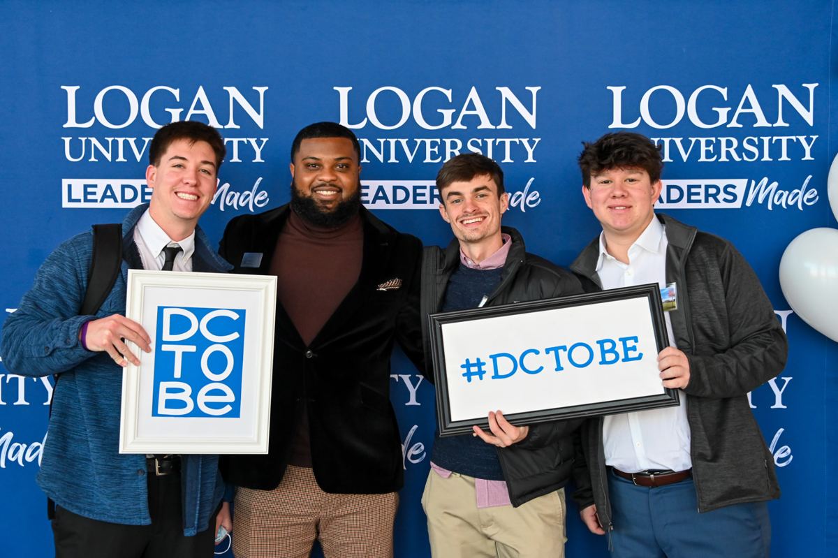 Four Logan students holding #DCTOBE signs at a campus admissions event