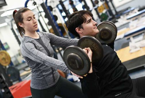 A Logan student spotting a classmate during a dumbbell press in the strength lab