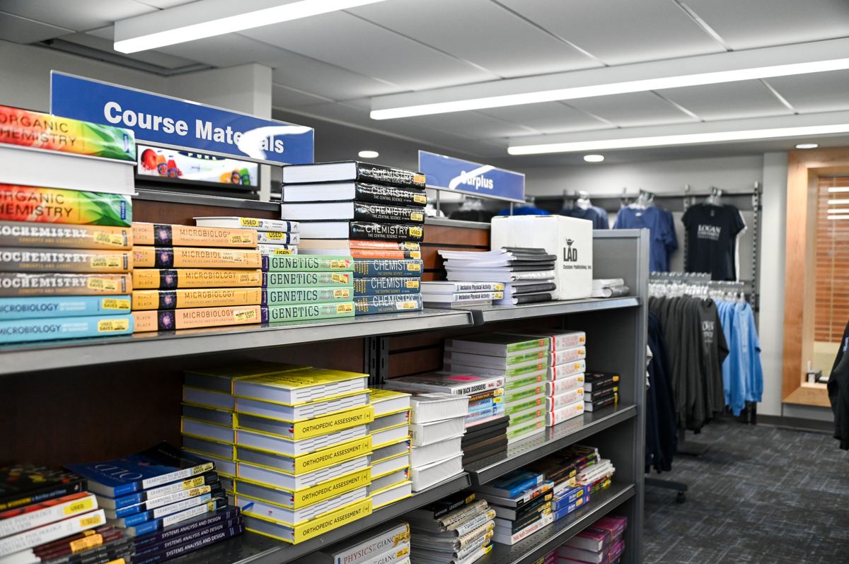 Course materials and textbooks shelved beside Logan University apparel in the campus bookstore.
