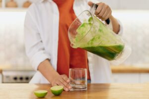 een vrouw giet een groene smoothie in een glas